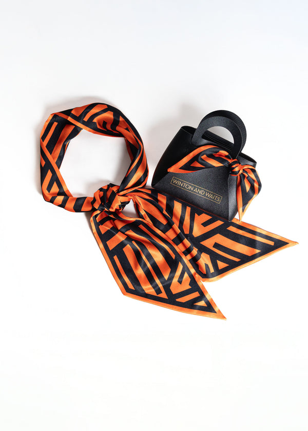 Orange and black patterned scarf with a black bag on a white background