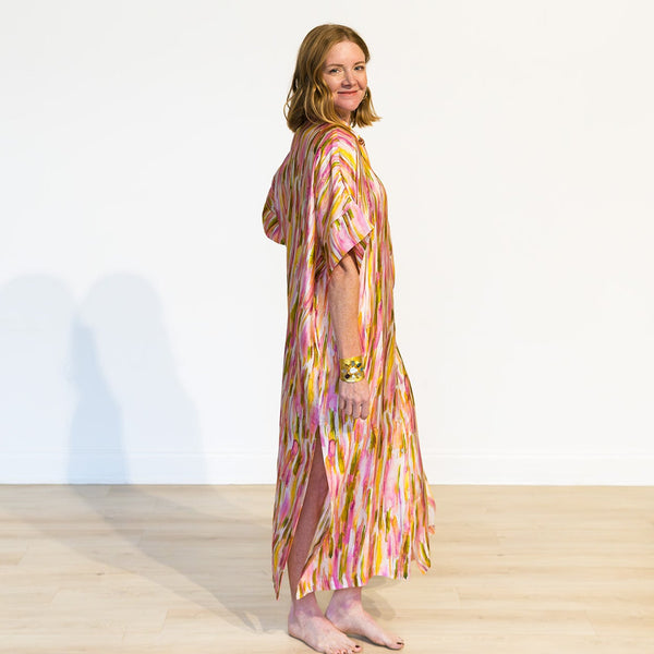 Woman wearing a colorful dress standing on a wooden floor with a white wall background