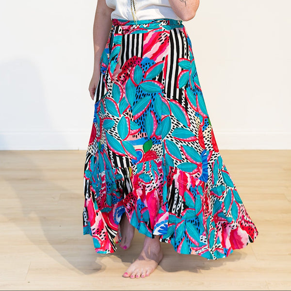 Woman wearing a colorful patterned skirt and white top on a plain background