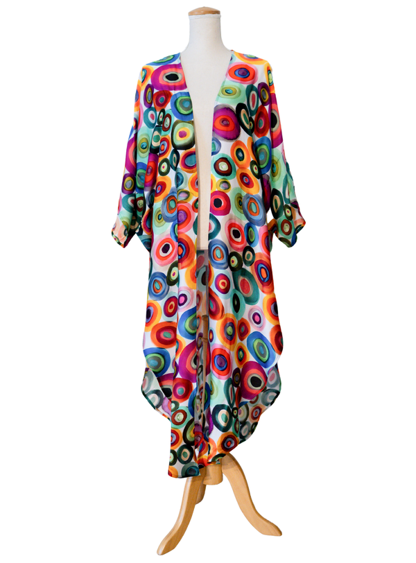 A long open-front kimono-style cover-up with three-quarter sleeves, displayed on a mannequin. The garment features a vibrant, all-over retro concentric circle pattern in multiple bright colors including orange, red, yellow, green, blue, purple, and black on a light base.