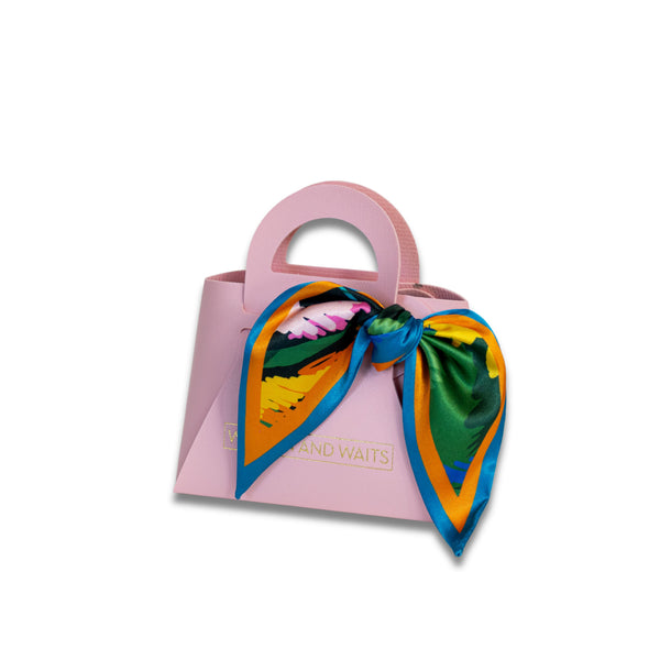 Small pink handbag with a colorful scarf tied around it on a white background