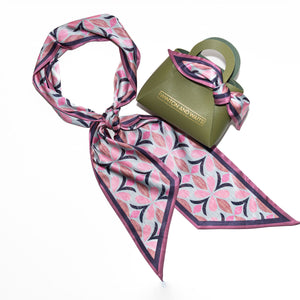 Pink and black patterned scarf draped over a green bag on a white background