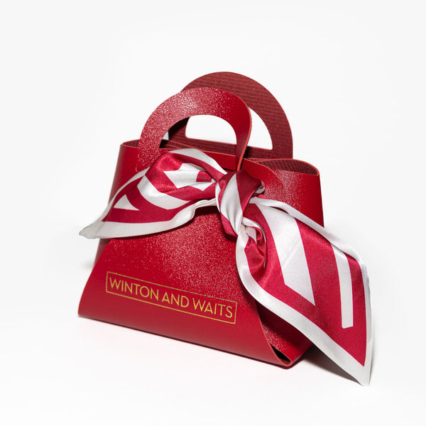 Red handbag with a white and red striped scarf tied around it on a white background, featuring 'Winton and Waits' branding.