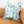 A linen euro pillow with a peacock and floral pattern, displayed on a brown sofa.