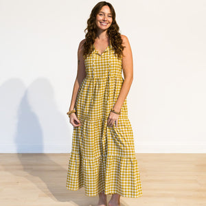 Woman wearing a yellow checkered dress standing against a white wall.