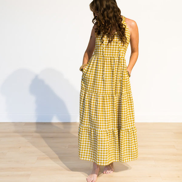 Woman wearing a yellow checkered dress standing on a wooden floor with a white wall background
