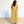 Woman wearing a yellow checkered dress standing against a white wall.