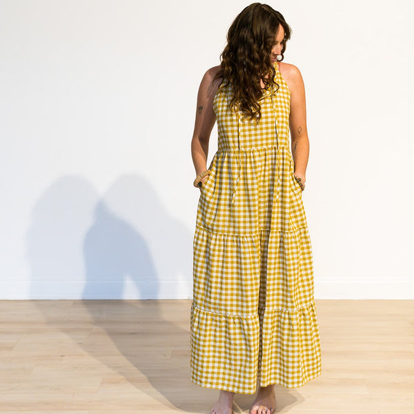 Woman wearing a yellow checkered dress standing against a white wall.