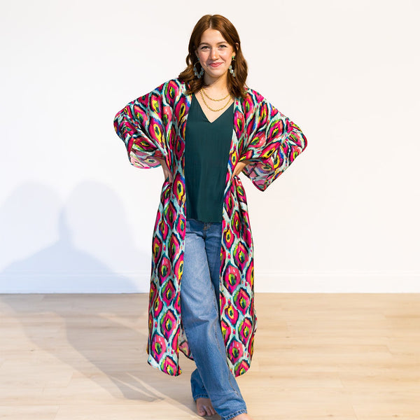 Woman wearing a colorful patterned kimono over a green top and blue jeans on a white background
