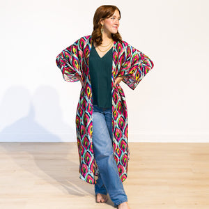 Woman wearing a colorful patterned kimono over a green top and jeans on a white background
