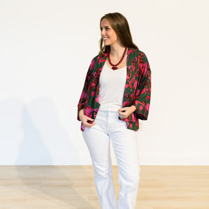 Woman wearing a floral jacket, white top, and white pants on a plain background