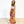 A woman wearing a white sleeveless top and a vibrant, multicolored floral maxi skirt stands in a studio setting with a plain white wall and light wood floor.