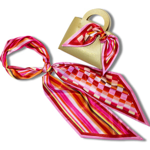 Gold handbag with a colorful scarf tied around it on a white background