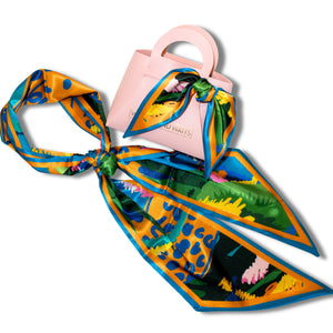 Colorful scarf with floral pattern draped over a pink handbag on a white background