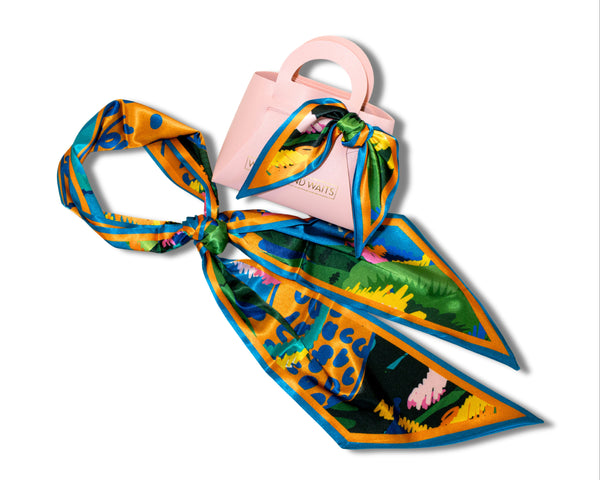 Colorful scarf with floral pattern draped over a pink handbag on a white background
