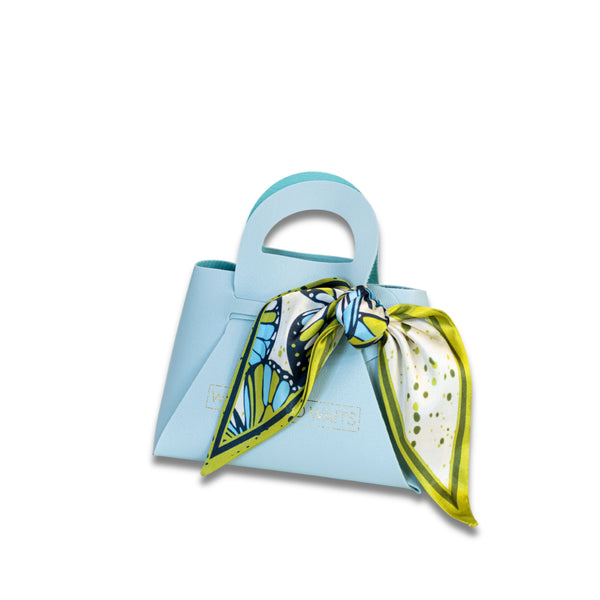 Small light blue handbag with a colorful scarf tied around it on a white background